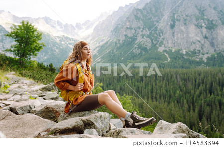 Happy woman with a yellow hiking backpack enjoying the mountain landscape. Travel concept. Happy woman with a yellow hiking backpack enjoying the mountain landscape. Travel concept. 114583394