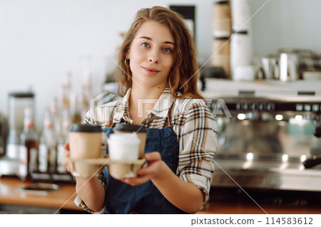 Portrait of beautiful young barista woman serving coffee with a big smile. Small business owner. Portrait of beautiful young barista woman serving coffee with a big smile. Small business owner. 114583612