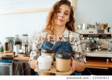 Portrait of beautiful young barista woman serving coffee with a big smile. Small business owner. 114583613