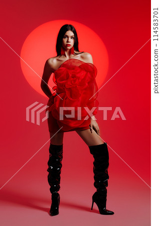 A young girl in a red dress posing in the studio against the backdrop of a red spotlight. A young girl in a red dress posing in the studio against the backdrop of a red spotlight. 114583701