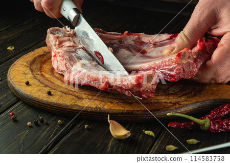 Slicing meat ribs with a knife in the hand of a butcher before preparing a barbecue. Concept of cooking meat dish on kitchen table in hotel 114583758