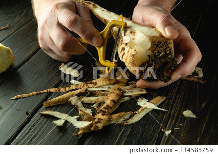 The chef peels raw sugar beet in a hotel kitchen before preparing a national dish. Close-up of a cook hands with a vegetable peeler while working 114583759