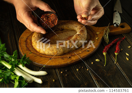 Cooking meat sausage. The cook hands add dry spices to the sausage for taste and aroma. Place for advertising on a black table 114583761
