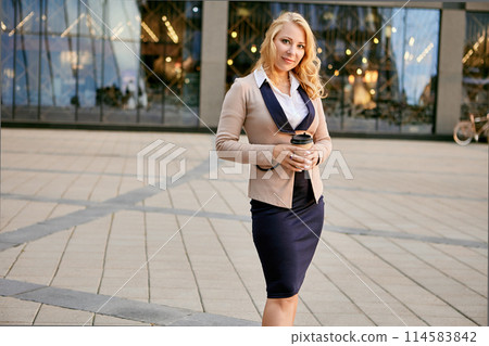 Businesswoman in suit with takeaway coffee stands near business center. 114583842