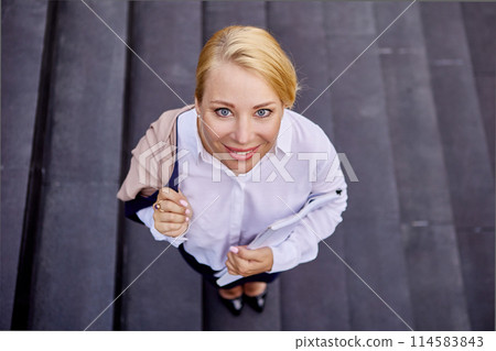 Cheerful blond woman is standing on stairs outside. 114583843