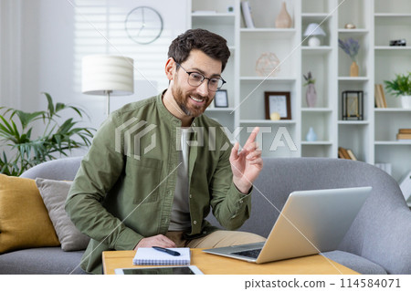 Smiling man conducting an online video class from his living room on a laptop, looking engaged and enthusiastic. Smiling man conducting an online video class from his living room on a laptop, looking engaged and enthusiastic. 114584071