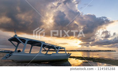 A boat rests on the sandy beach as the sunset over the horizon A boat rests on the sandy beach as the sunset over the horizon 114585288