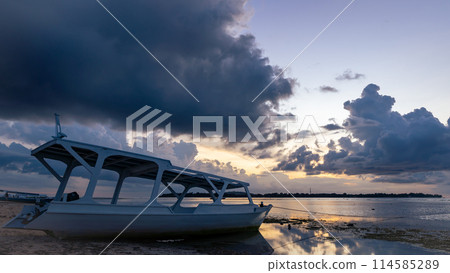 A boat rests on the sandy beach as the sunset over the horizon A boat rests on the sandy beach as the sunset over the horizon 114585289