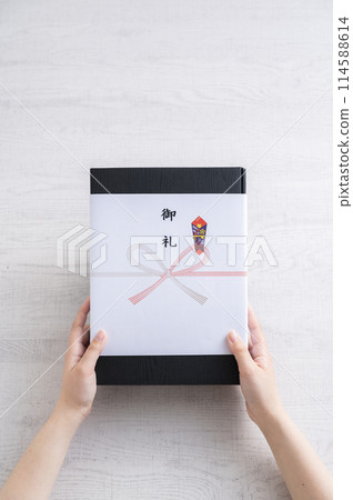 一位女士的手遞出一份覆蓋著 noshi 的禮物作為感謝 114588614