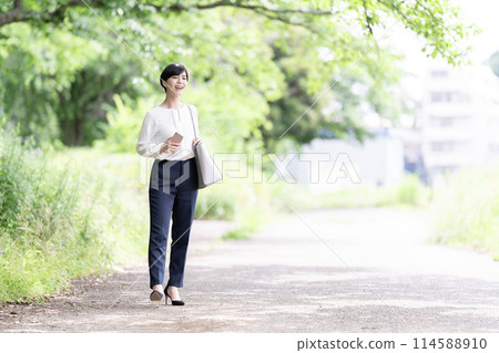 走在一條新鮮的綠色路的一個年輕女商人 走在一條新鮮的綠色路的一個年輕女商人 114588910