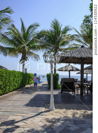 The boy runs to the beach to the sea along a wooden path past a lantern and palm trees The boy runs to the beach to the sea along a wooden path past a lantern and palm trees 114588922