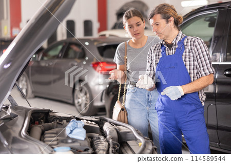 Mechanic consults woman on repairs under hood of car Mechanic consults woman on repairs under hood of car 114589544