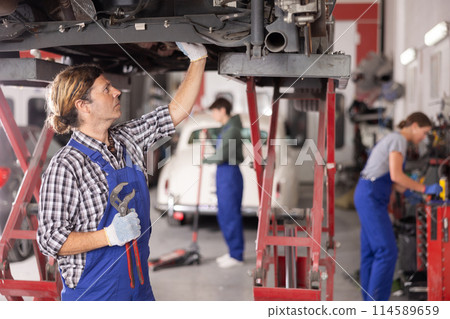 Experienced auto mechanic doing an inspection of rear suspension of a car in car service center 114589659