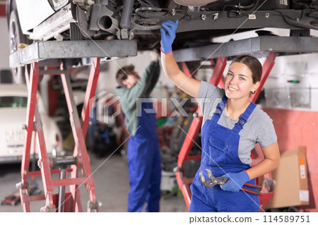 Female mechanic checking the rear suspension shock absorber of car Female mechanic checking the rear suspension shock absorber of car 114589751