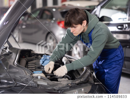 Young auto mechanic adjusting parts under hood of vehicle Young auto mechanic adjusting parts under hood of vehicle 114589833