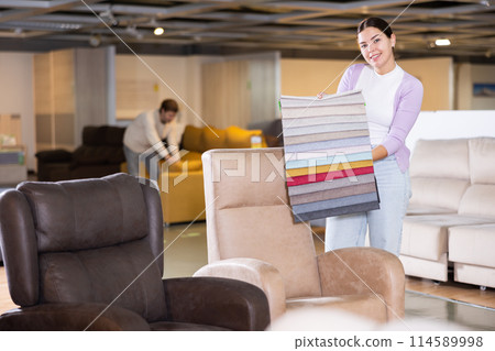 Female furniture salesperson showing different fabric samples in furniture showroom 114589998