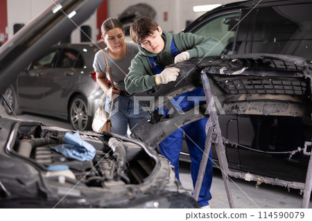 An auto mechanic shows a woman what problem is with her car bumper 114590079