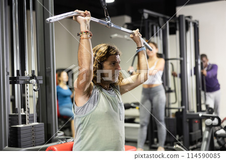 Caucasian man training on lat pull down machine in gym Caucasian man training on lat pull down machine in gym 114590085