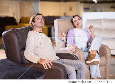 Man and woman sitting around in armchairs in furniture store 114590120