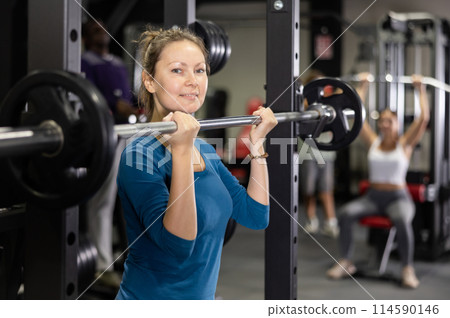 Caucasian woman doing exercises usining barbell and half rack in gym 114590146