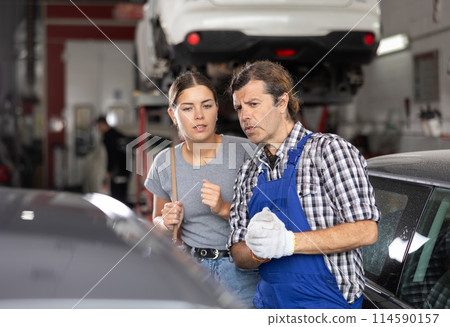 Worried woman talks about the problems of her car to an auto mechanic at car service center 114590157