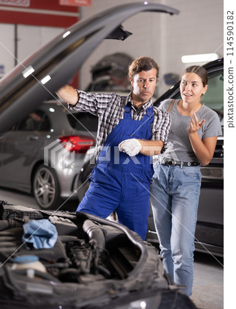 Female customer discussing engine repairs with experienced mechanic in workshop 114590182