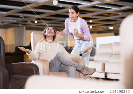 Happy couple trying out armchairs in furniture showroom 114590223