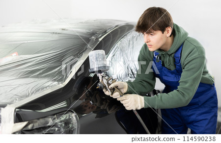 Young guy mechanic paints car with machine 114590238