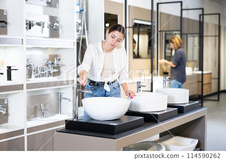 in plumbing department,thoughtful woman inspects round white ceramic sinks with faucets 114590262