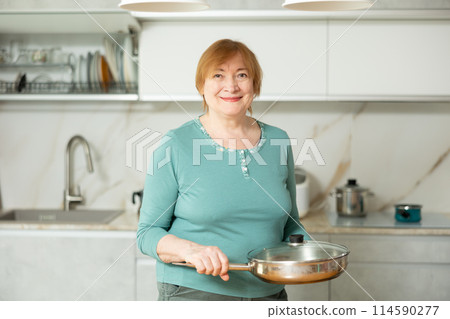 Portrait of a mature smiling woman with a frying pan in her hands Portrait of a mature smiling woman with a frying pan in her hands 114590277