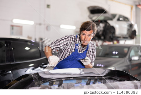 Man prepares car for painting in workshop - grinds and puts putty on bumper before painting 114590388