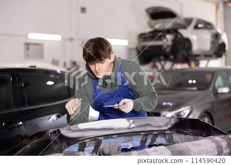Young guy mechanic repairs car with putty and spatula Young guy mechanic repairs car with putty and spatula 114590420