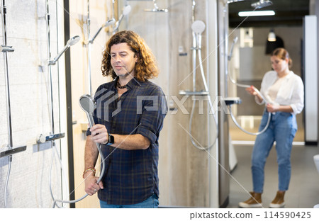 in plumbing department,man examines shower head and quality of metal coating. 114590425