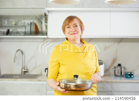 Adult woman posing with frying pan in kitchen Adult woman posing with frying pan in kitchen 114590456