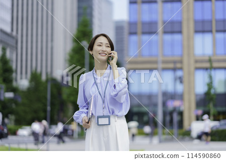 A businesswoman standing in an office district talking on a smartphone A businesswoman standing in an office district talking on a smartphone 114590860