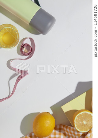 White countertop containing many items of weight losing flat lay above such as measuring tape, lemon ingredient, water and so on. Vacant space in center for showing product, top view 114591726