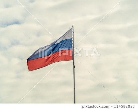 Russian tricolor flag waving in the wind against a blue sky. 114592053