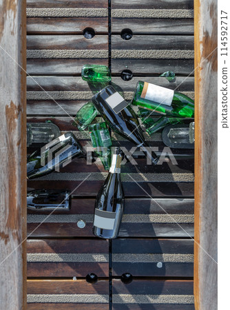 Top view of The beer and wine bottles were left on the floor next to the wooden benches 114592717