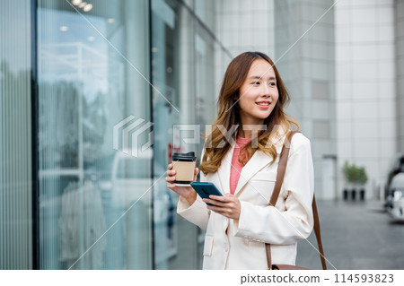 Busy businesswoman juggling coffee and cell phone, staying connected while walking to work in the morning. 114593823