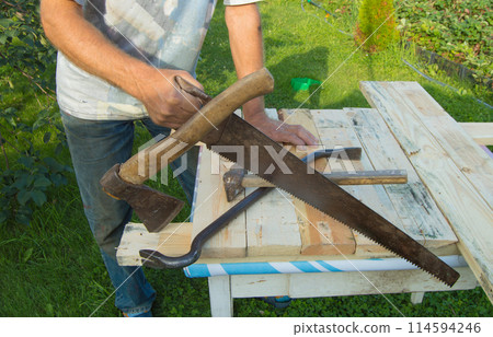man uses a hacksaw, a hatchet, a claw hammer for construction work in your garden 114594246