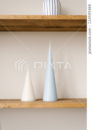 Blue and white taper candle on a wooden shelf in a Scandinavian minimalist style living room 114595468