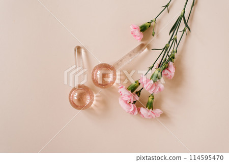 Two pink glass spheres for facial massage with pink liquid in them lie on the table next to a bouquet of pink carnation flowers 114595470