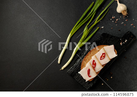 sandwich with lard and red pepper on a black cutting board on a black background 114596875
