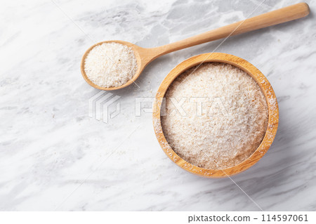 Psyllium husk in wood bowl and spoon on white marble table, top view, copy space 114597061