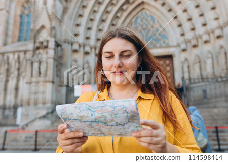 Young woman tourist with paper map standing in front of the famous saint Eulalia church in Barcelona. Concept of travel, tourism and vacation in city. Cathedral of Barcelona Young woman tourist with paper map standing in front of the famous saint Eulalia church in Barcelona. Concept of travel, tourism and vacation in city. Cathedral of Barcelona 114598414