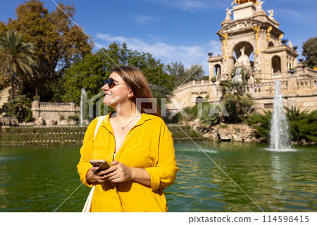 Young female tourist with phone visiting Ciutadella Park in Barcelona. Concept of travel, tourism and vacation in city. Use technology concept, Traveling Europe Young female tourist with phone visiting Ciutadella Park in Barcelona. Concept of travel, tourism and vacation in city. Use technology concept, Traveling Europe 114598415