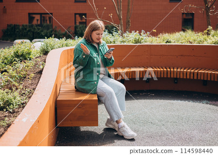 Perplexed woman holding cellphone in hands on the street in summer, looking at screen with irritated expression, made a mistake or annoyed by texts and calls. Negative emotion. High quality photo Perplexed woman holding cellphone in hands on the street in summer, looking at screen with irritated expression, made a mistake or annoyed by texts and calls. Negative emotion. High quality photo 114598440