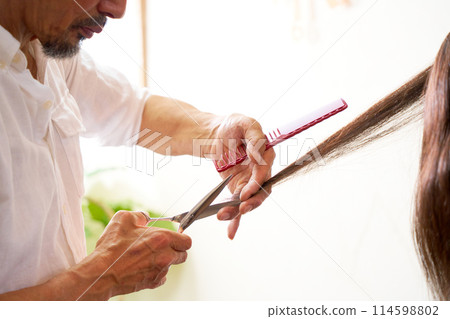 The hands of a veteran hairdresser cutting hair 114598802