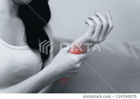 Closeup of woman sitting on sofa holds her wrist, hand injury with red highlight 114598876