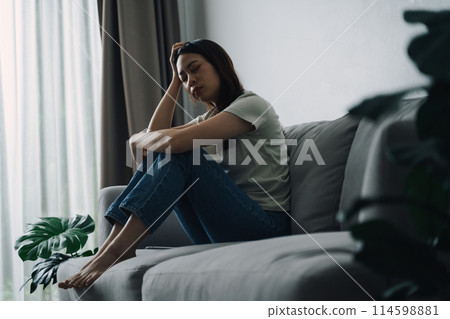 Unhappy lonely depressed woman is sitting on the couch and holding her head. Unhappy lonely depressed woman is sitting on the couch and holding her head. 114598881
